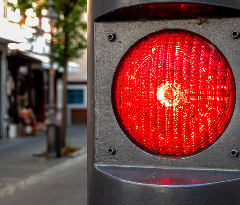 Blitzerprofis - roter Blitzer steht im Vordergrund und hinten ist eine kleine EInkaufsstraße zusehen